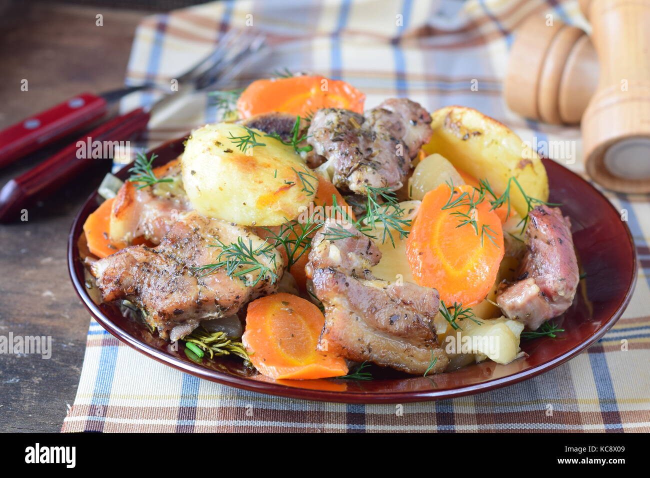Oven cooked pork with potato, carrots and onion in olive oil and spices in a brown ceramic plate on a wooden background. Home cooking Stock Photo