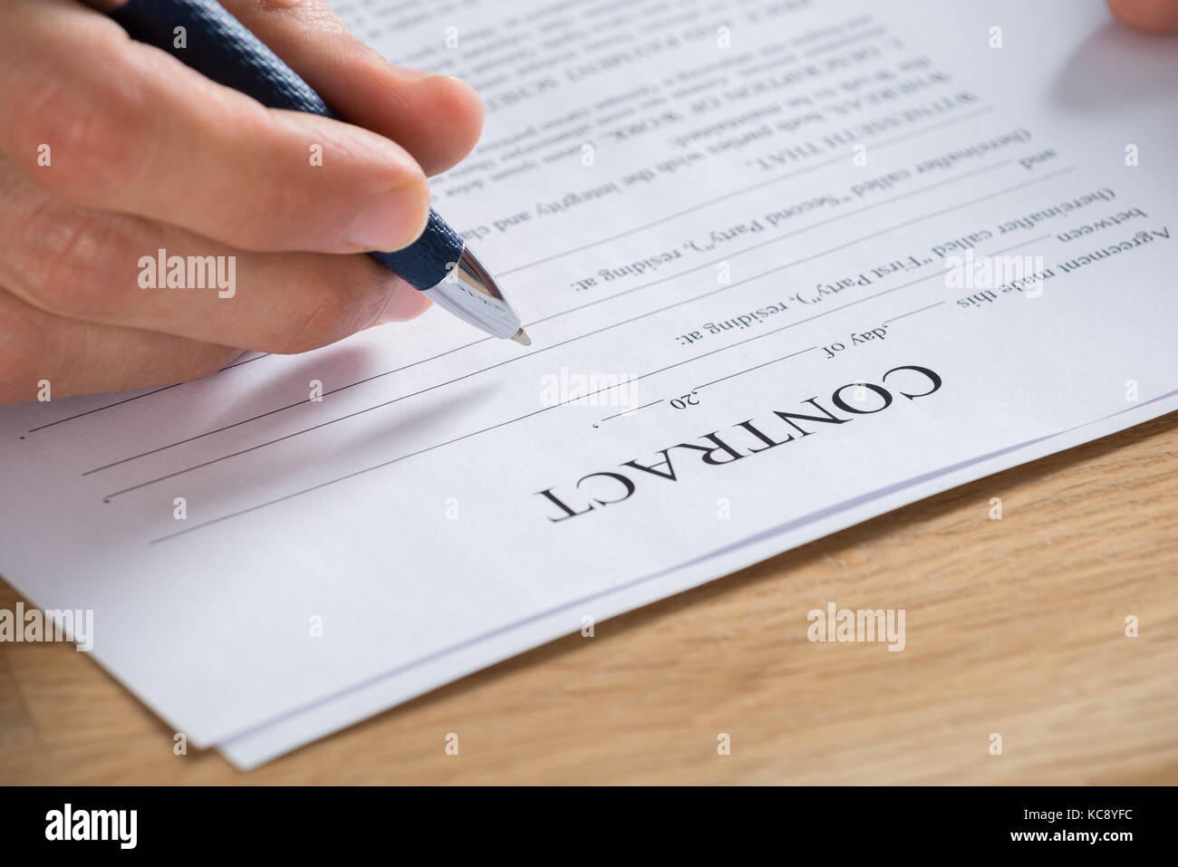 Close-up Of Businessman Hand Holding Pen On Contract Paper At Wooden Desk In Office Stock Photo