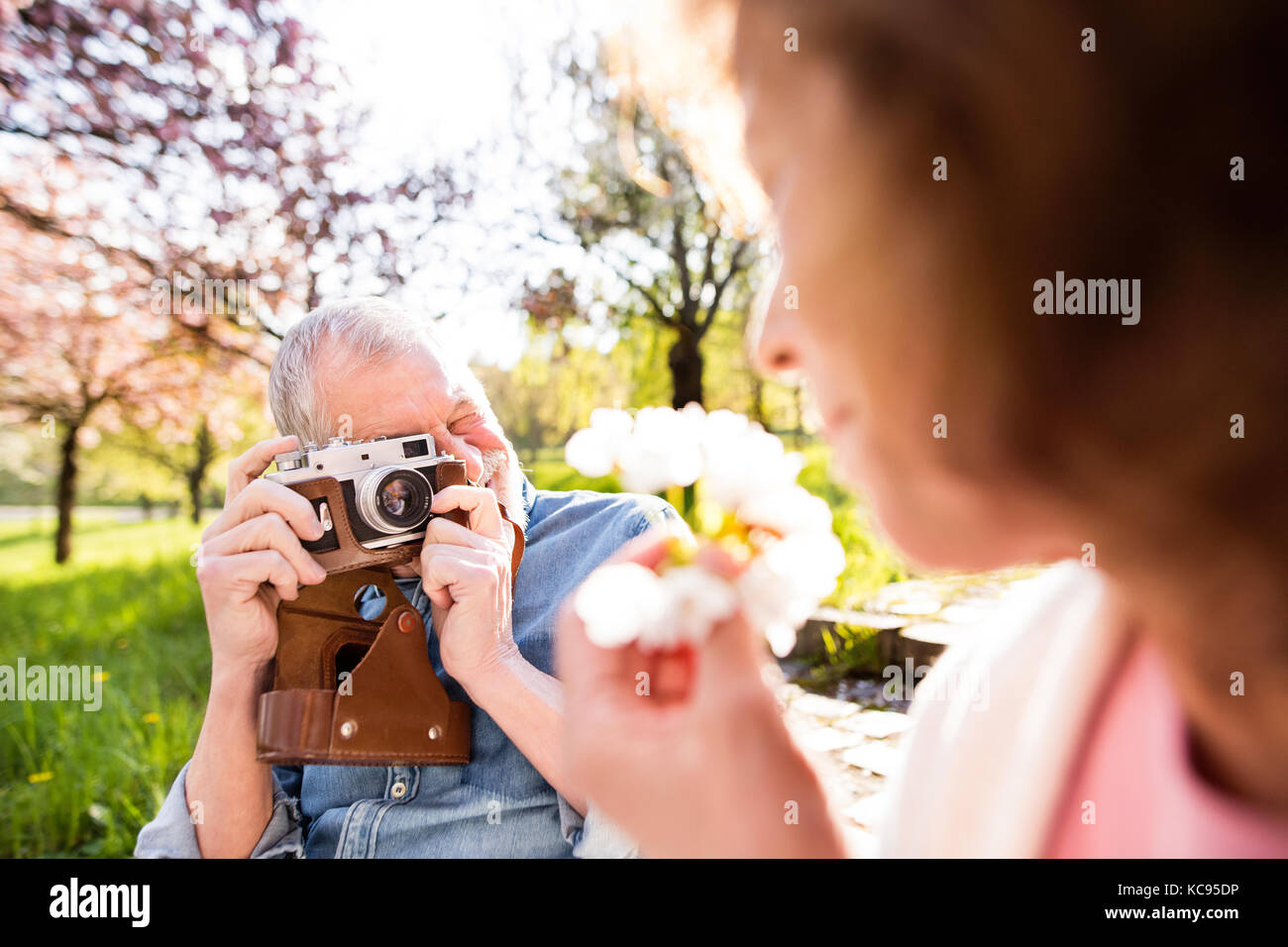 Beautiful senior couple in love outside in spring nature. Man with camera taking a picture of a woman. Stock Photo