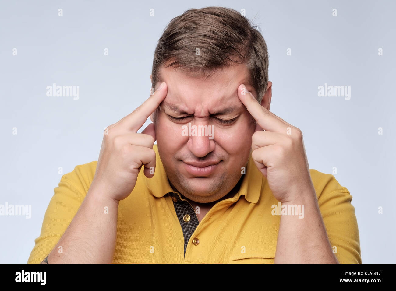 Stressed fat man in yellow t-shirt with fingers on temple suffering from headache. Stock Photo
