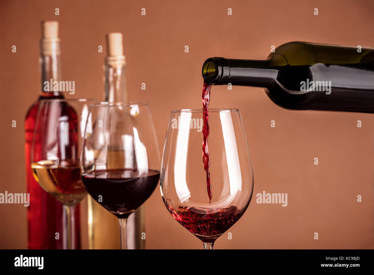 Red wine being poured into a glass from a bottle, on a dark background, with copy space and other glasses and more bottles in the blurred background.  Stock Photo