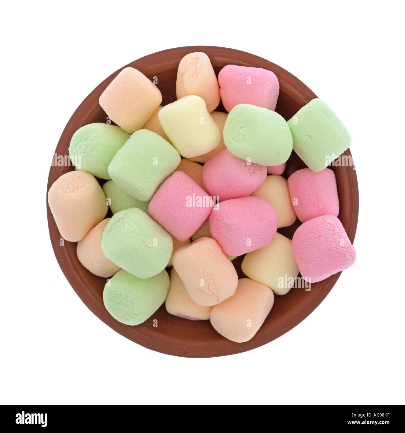 Top view of a small red clay bowl filled with colorful pastel hued miniature green, pink, yellow and orange marshmallows isolated on a white backgroun Stock Photo