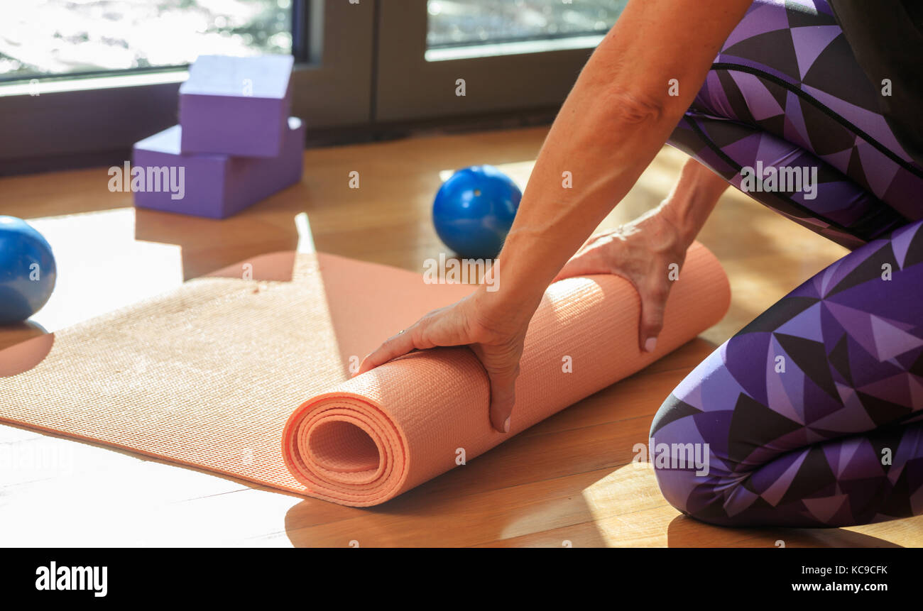 Fitness at home concept. Woman rolling an exercise mat on wooden floor ...