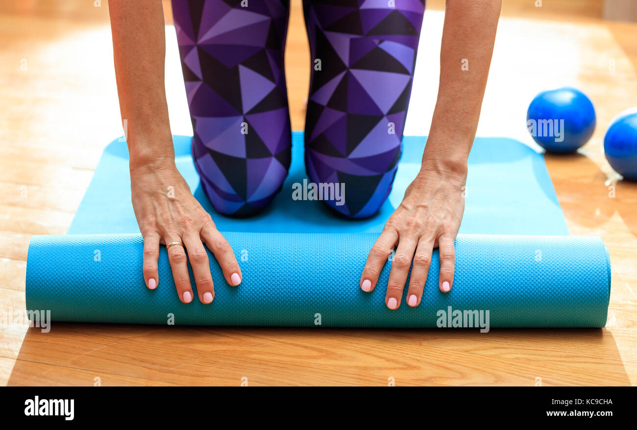 Fitness at home concept. Woman rolling an exercise mat on wooden floor ...