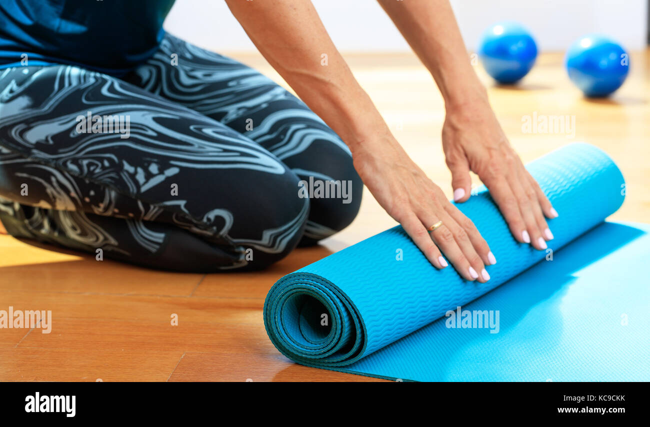 Fitness at home concept. Woman rolling an exercise mat on wooden floor ...