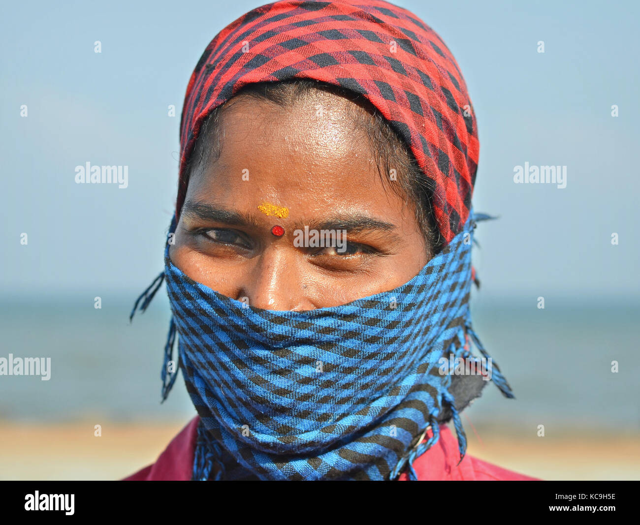 Young Tamil low-caste female street sweeper, covering her nose and mouth with a blue-and-black checkered dust bandana Stock Photo