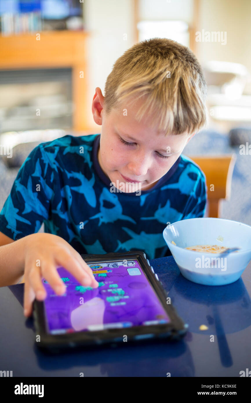 Avon, Outer Banks, North Carolina, USA.  Pre-teenage American Boy Eating Breakfast while Playing on his  Mobile Game Device. Stock Photo
