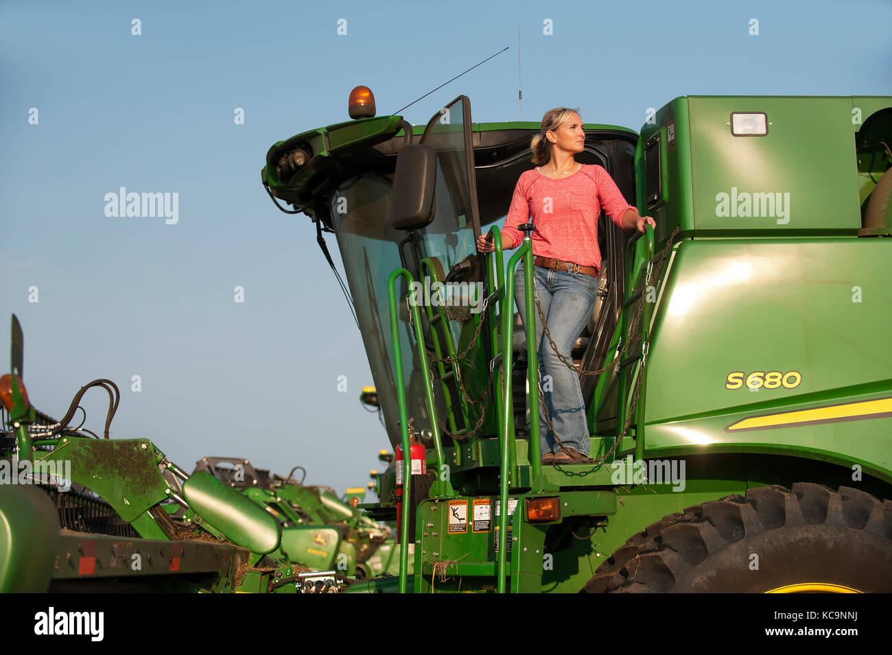 A YOUNG FEMALE FARMER LOOKS OUT OVER THE FIELD FROM HER JOHN DEERE