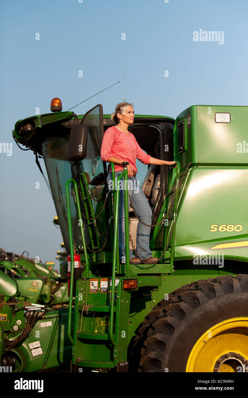 A YOUNG FEMALE FARMER LOOKS OUT OVER THE FIELD FROM HER JOHN DEERE