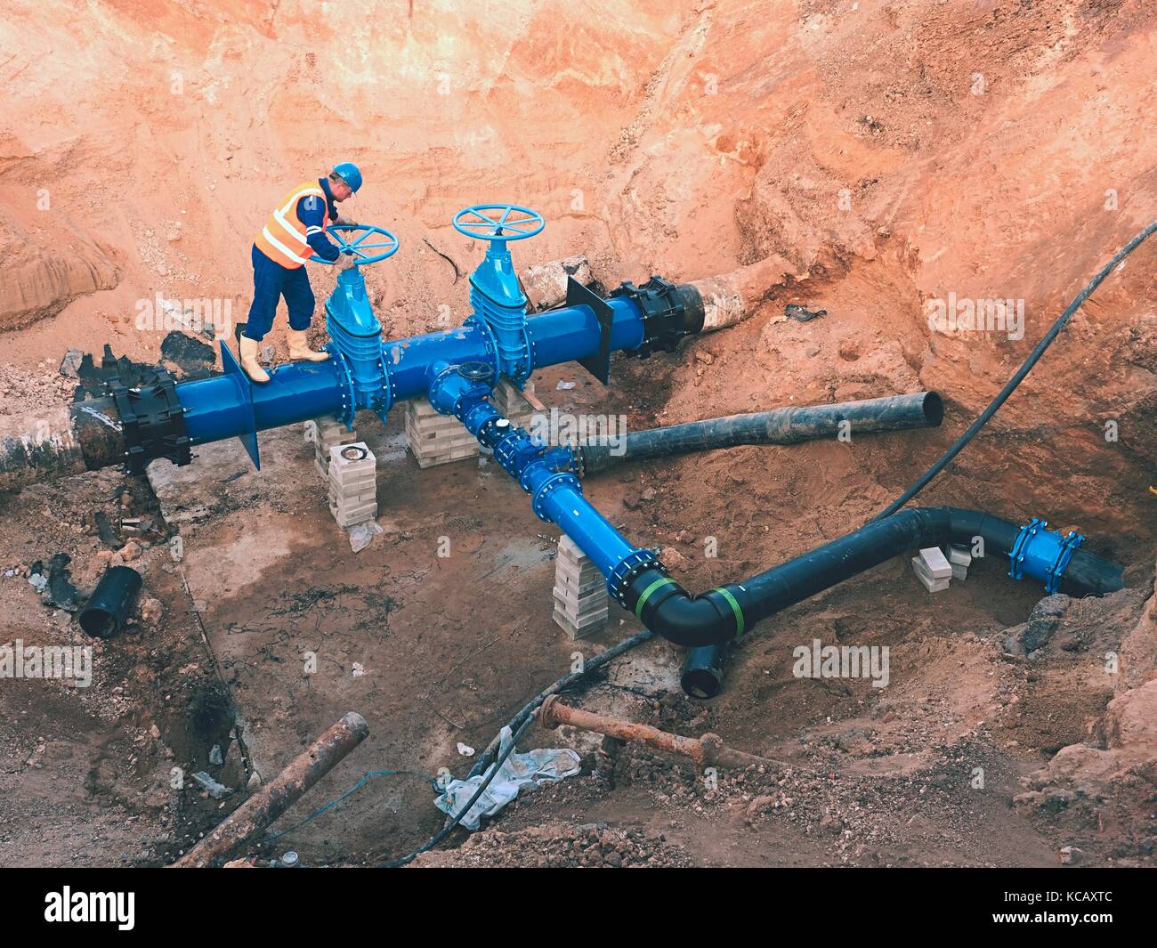 Worker in safety clothes drive valve conduit  on City potable water pipe  joined with black multi coupler into old pipeline system. Con Stock Photo