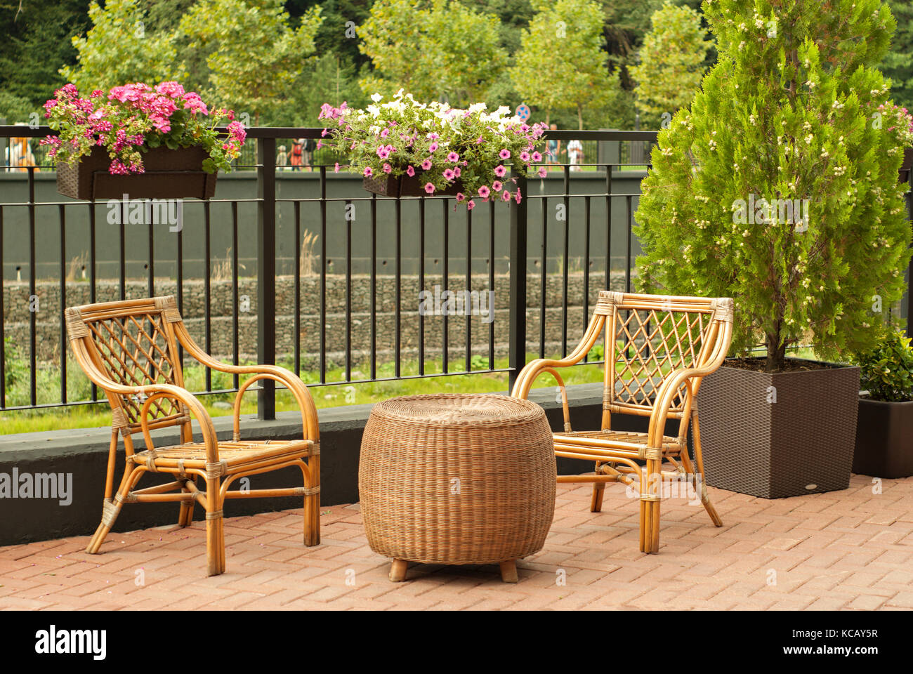 wicker outdoor furniture - two chairs and a round table - stand on the pedestrian promenade of a small river on a sunny day Stock Photo