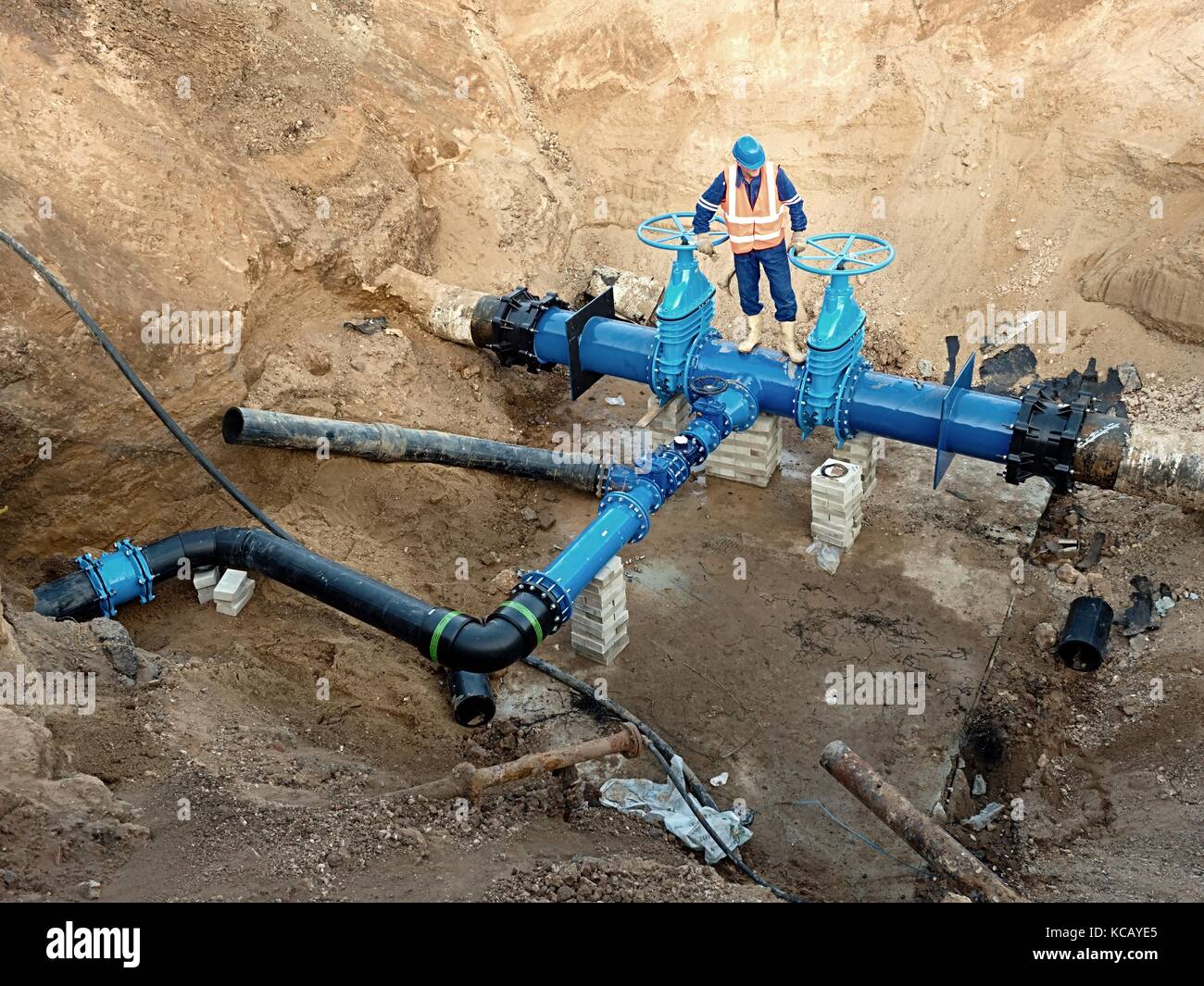 Technical expert open gate valve on 500mm drink water pipes joined with new black member eccentric fastener into old pipeline system. Man control Stock Photo