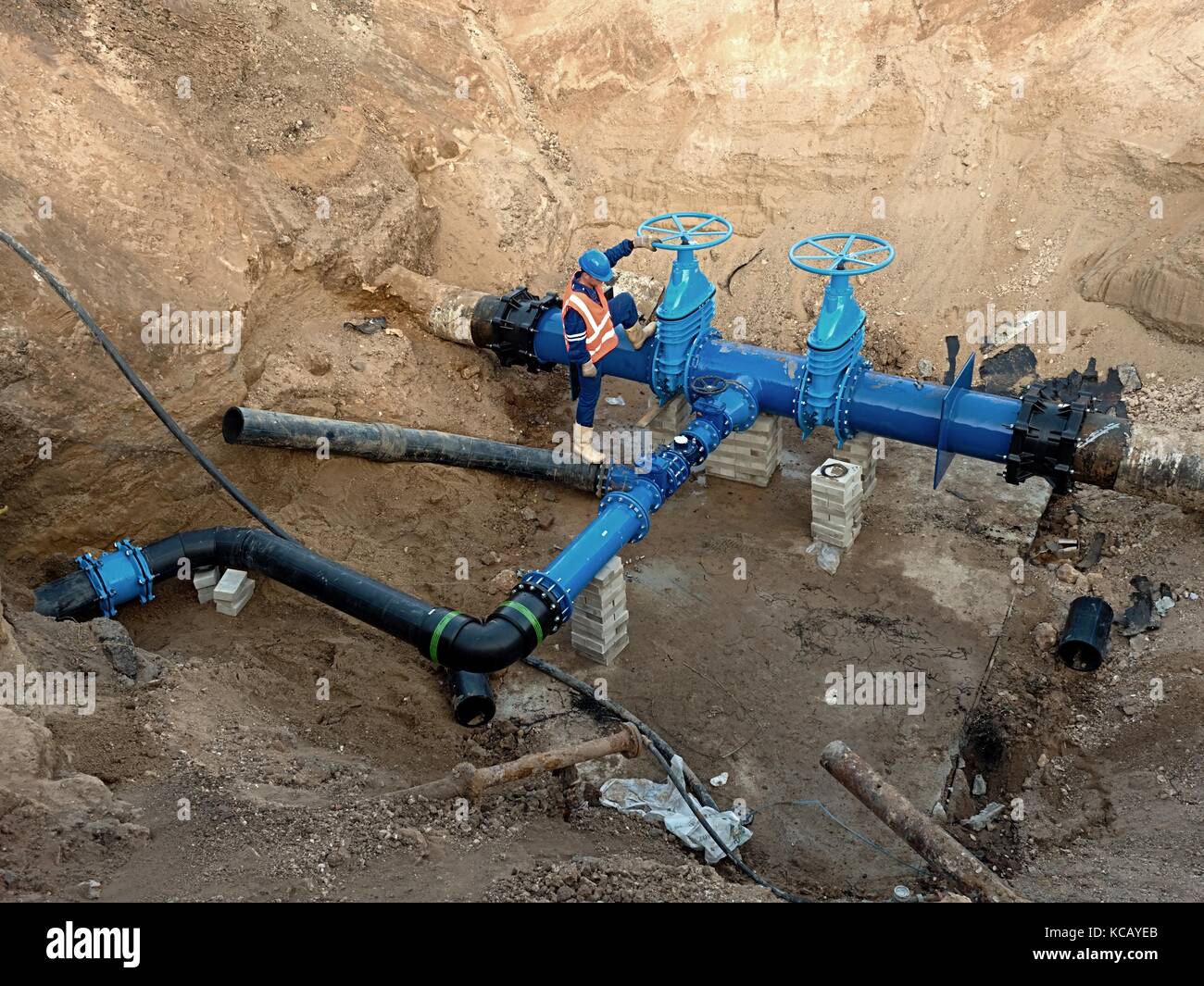 Technical expert underground at  gate valve on 500mm drink water pipes joined with new black multi axes eccentric fastener into old pipeline system. Stock Photo
