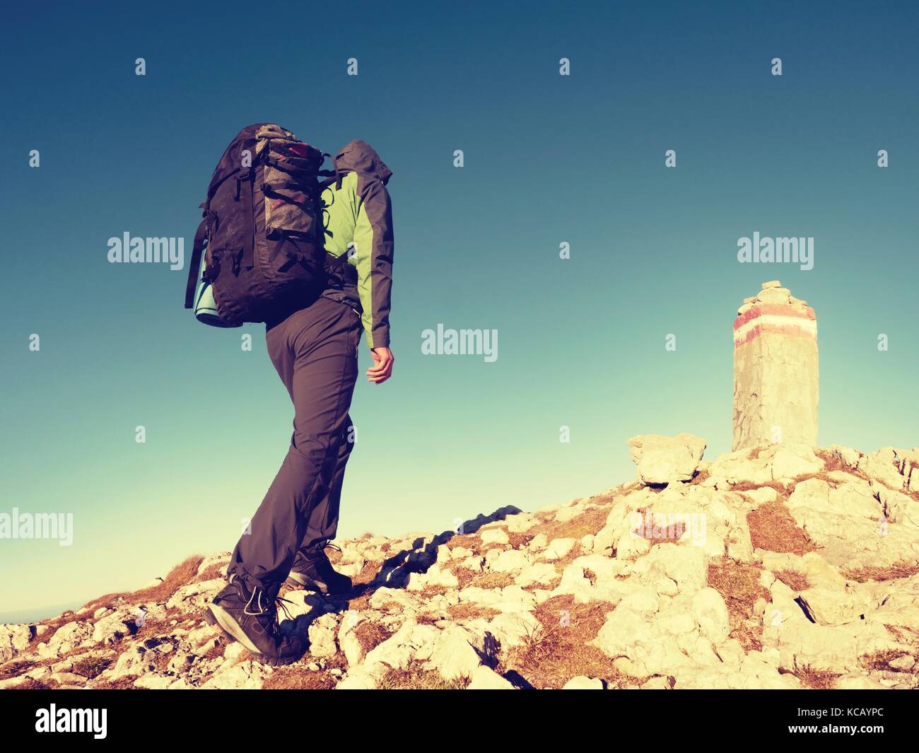 Hiker with backpack climbing on mountain peak. Summit stone at Alps