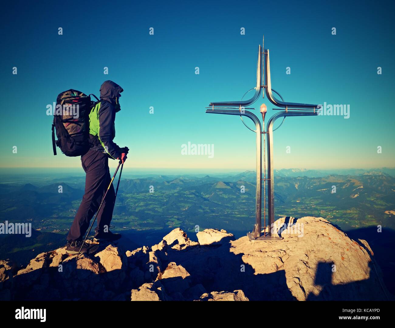 Hiker at big crucifix on mountain peak. Iron cross at Alps mountain top