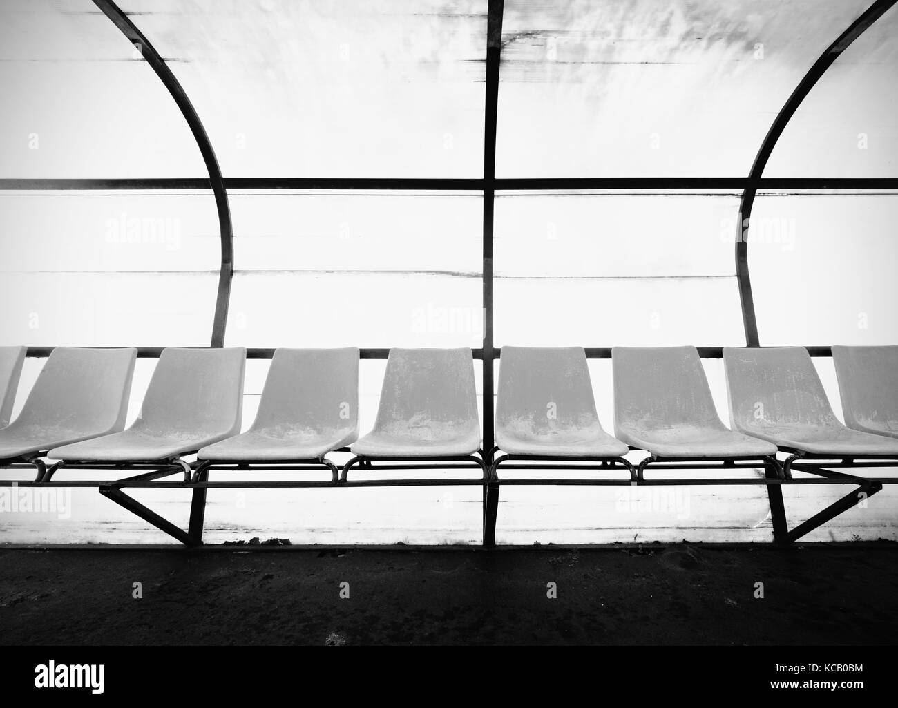 Vintage plastic seats on outdoor stadium players bench, chairs with worn paint below yellow roof. Stock Photo