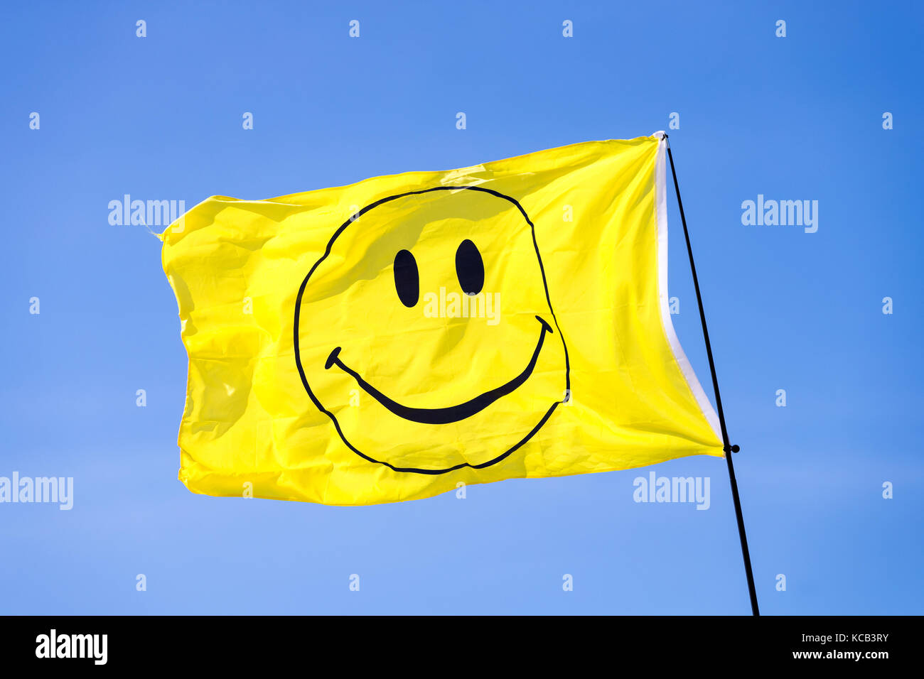 A yellow smiley face flag blowing in the wind against a blue sky Stock Photo