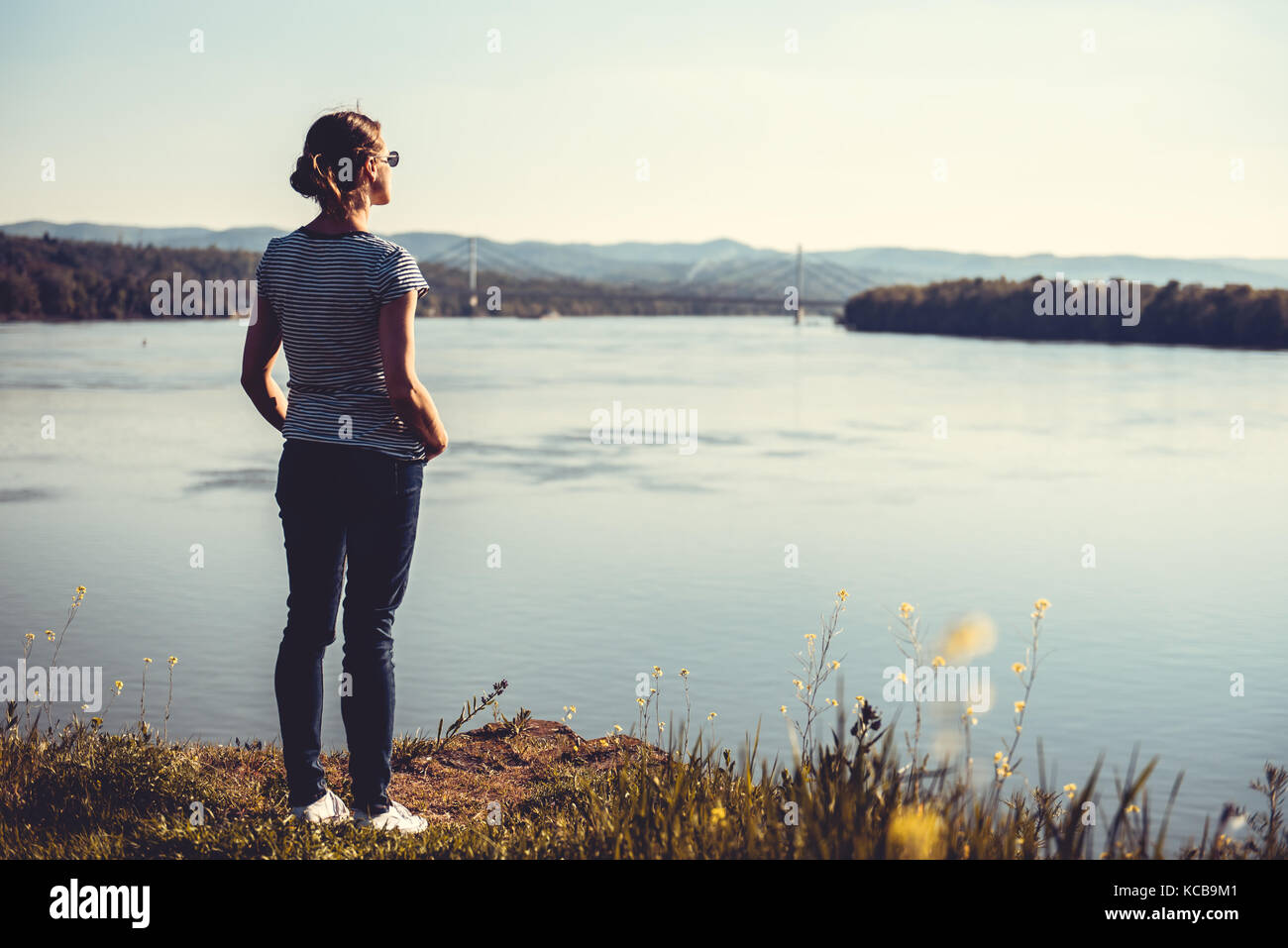 Woman standing by river and looking at the sun Stock Photo - Alamy