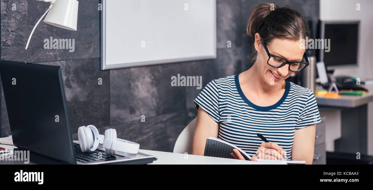 Woman wearing eyeglasses working late at the office and writing Stock Photo