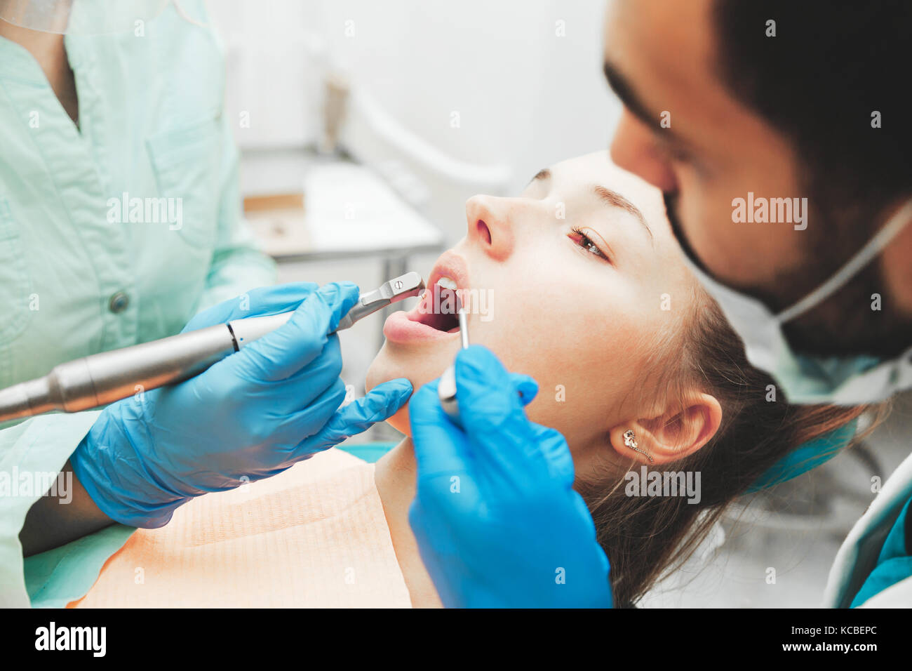 Dentists using dental drill and sucker while examining girl's mouth in ...