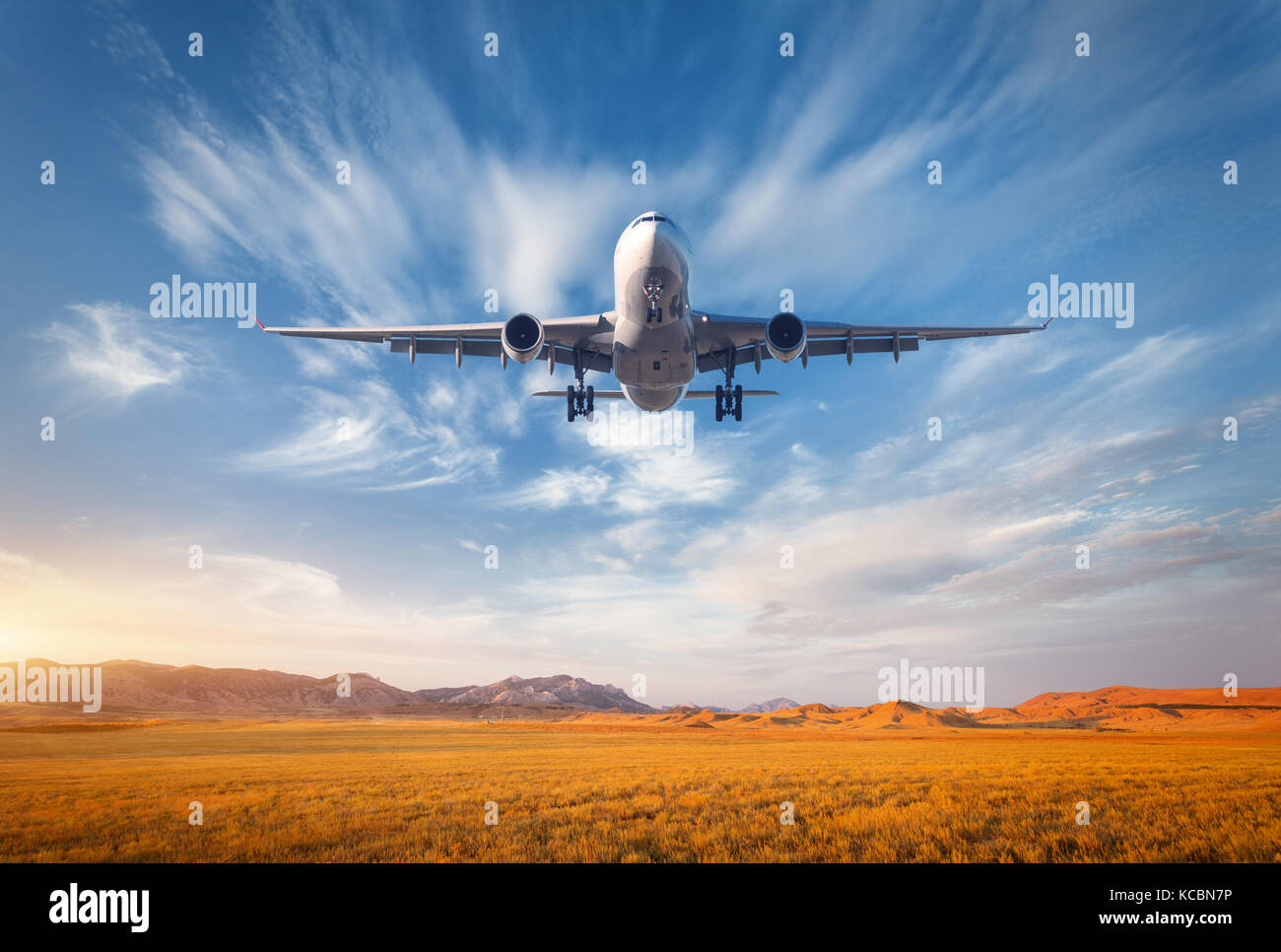 Airplane. Colorful landscape with passenger airplane is flying in the blue sky with clouds over grass field in mountain valley at sunset in summer. Pa Stock Photo