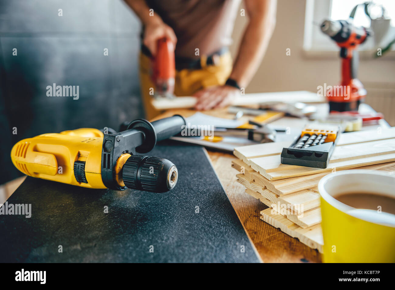 Yellow power drill and man using electric Jigsaw on the table with