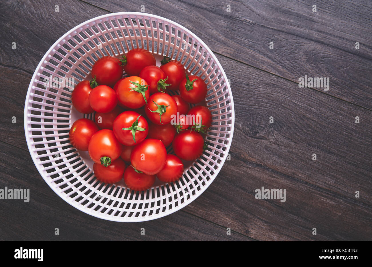 Fresh ripe red tomatoes in a colander on a dark wood work surface, worktop background Stock Photo