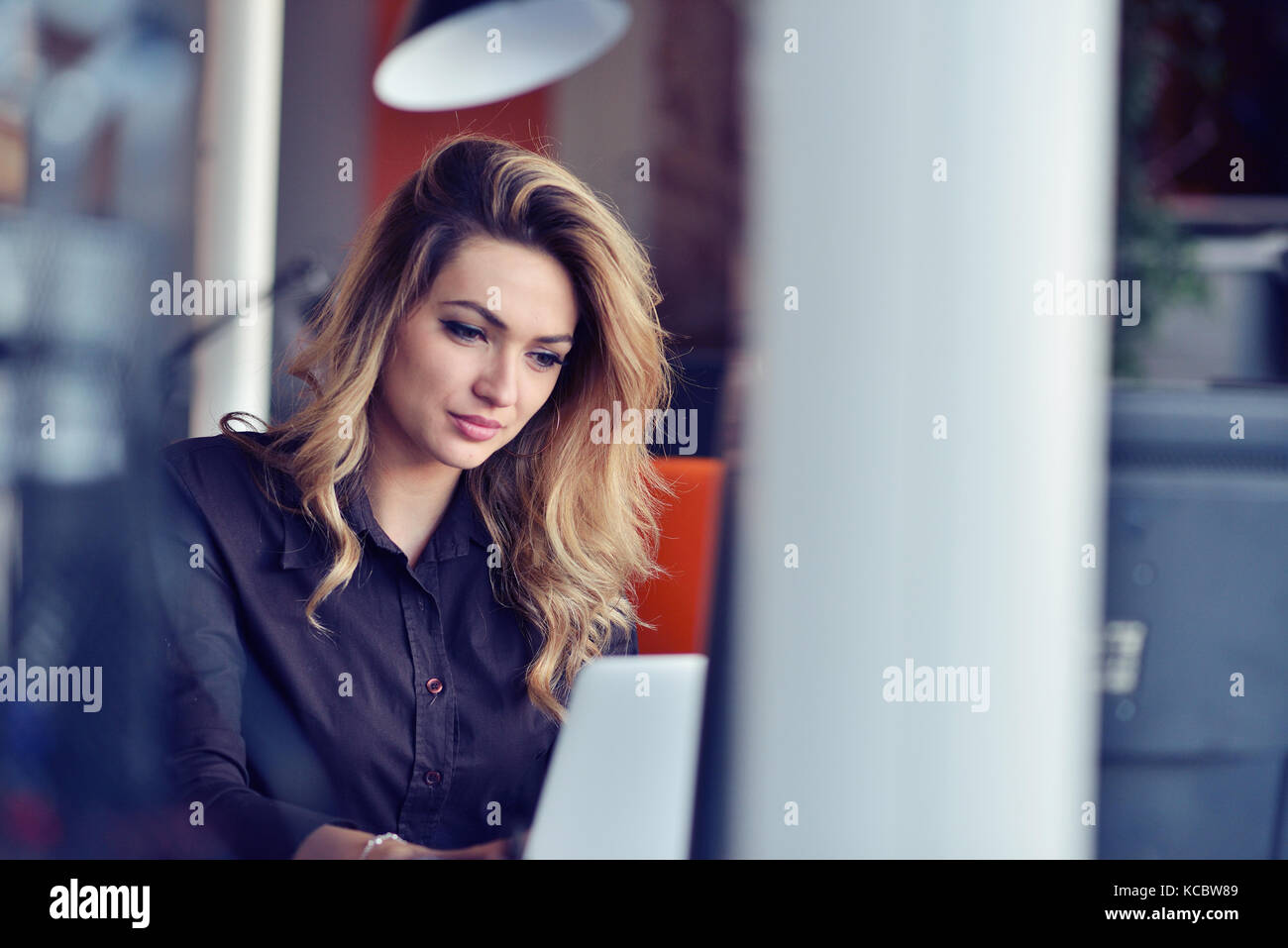 Portrait of smiling pretty young business woman sitting on workplace ...