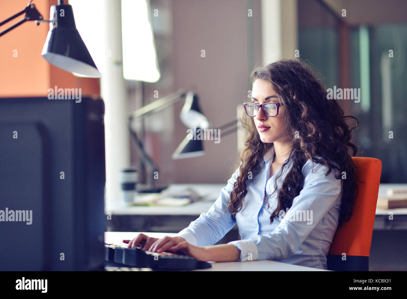 Portrait of smiling pretty young business woman in glasses sitting on ...