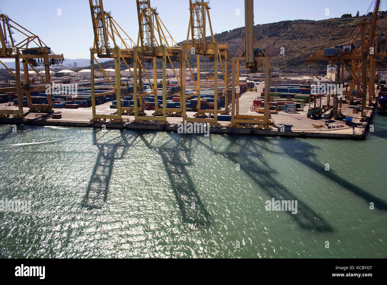 Aerial view of shadows of big, giant cranes on sea surface at Barcelona port. Many containers are in the background. Stock Photo