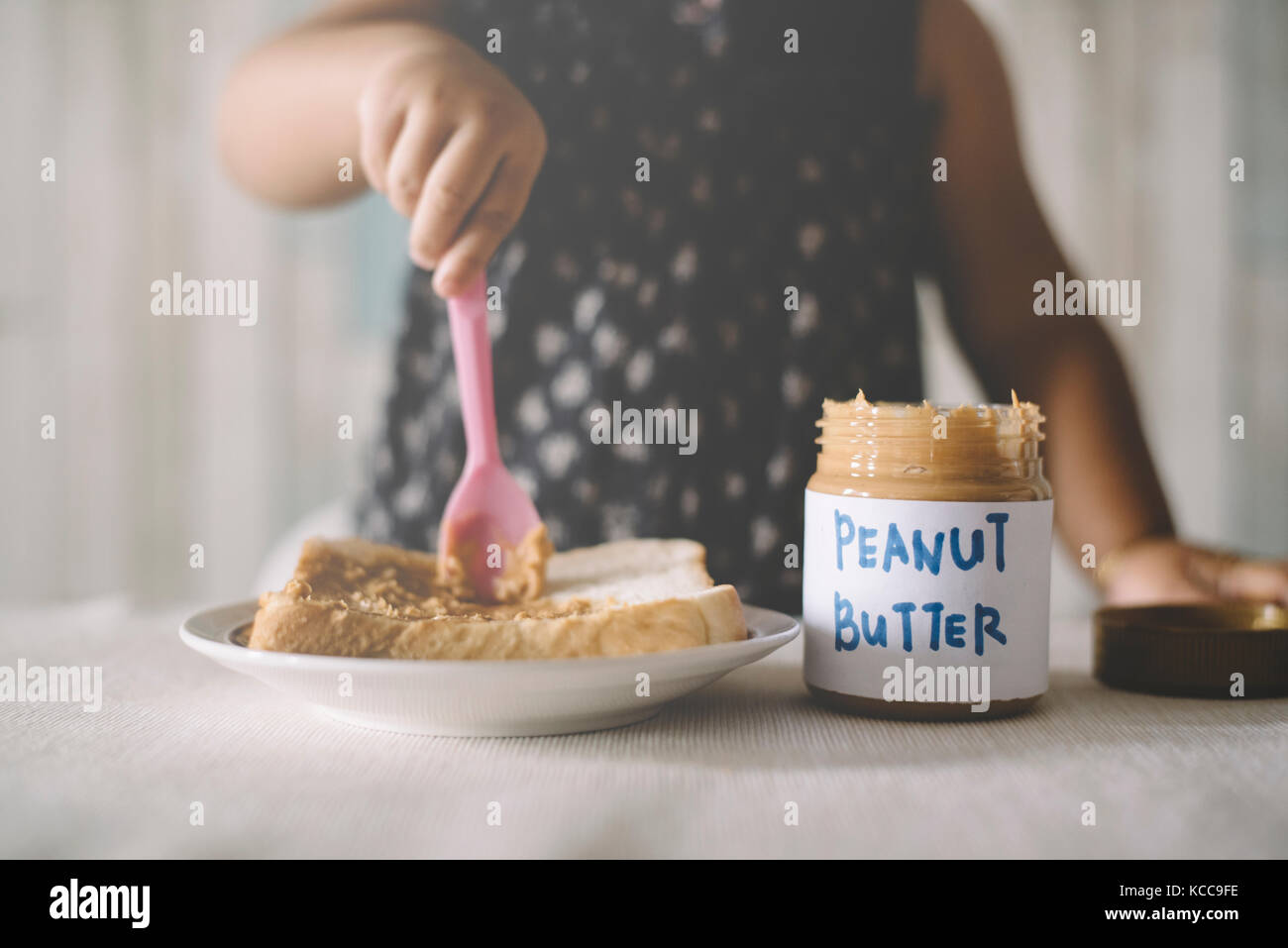 Asian Baby girl playing / spreading peanut butter on a bread. Baby making a mess with peanut butter Stock Photo