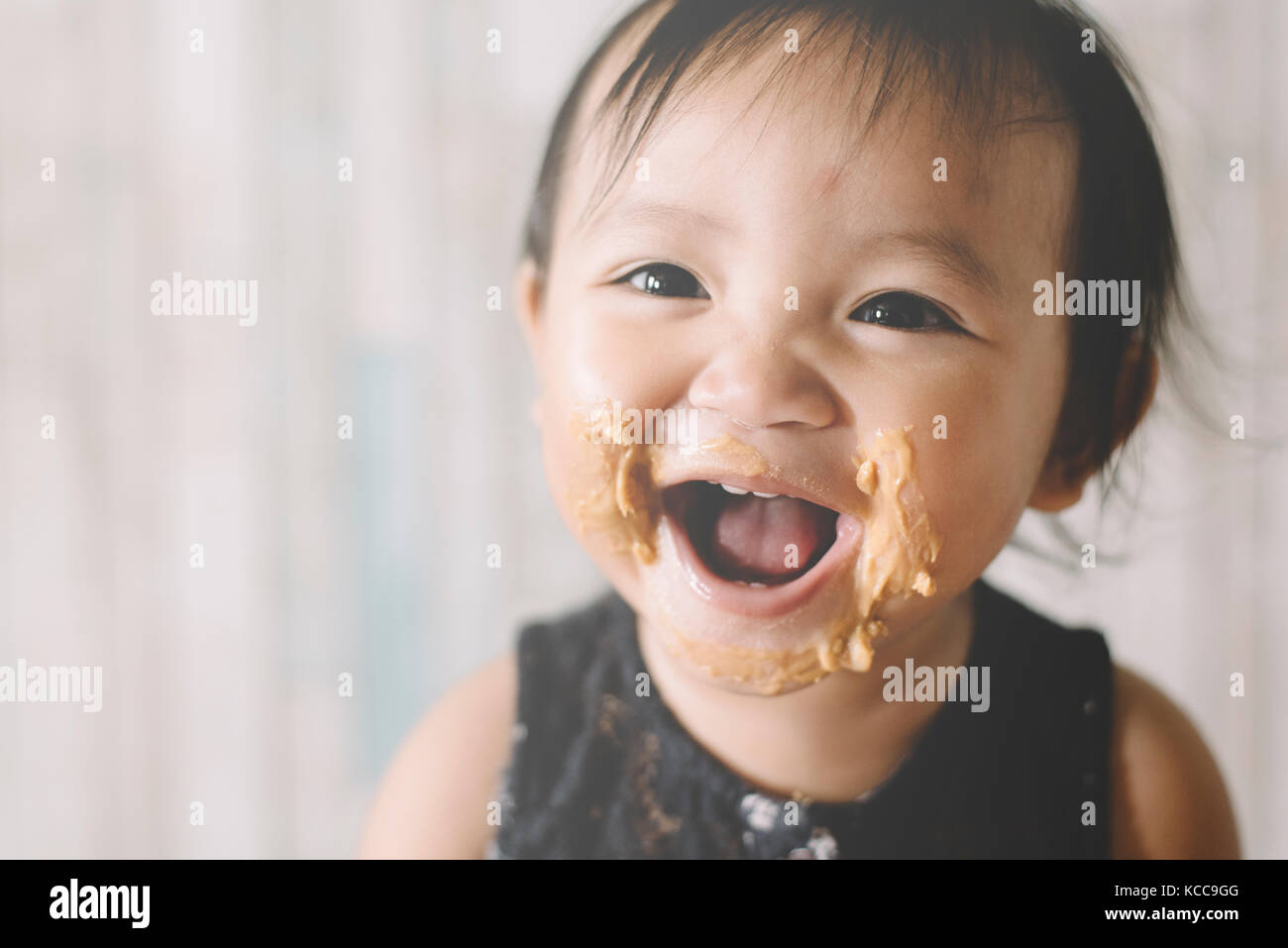 Asian Baby girl smiling with mouth and face full of peanut butter Stock Photo