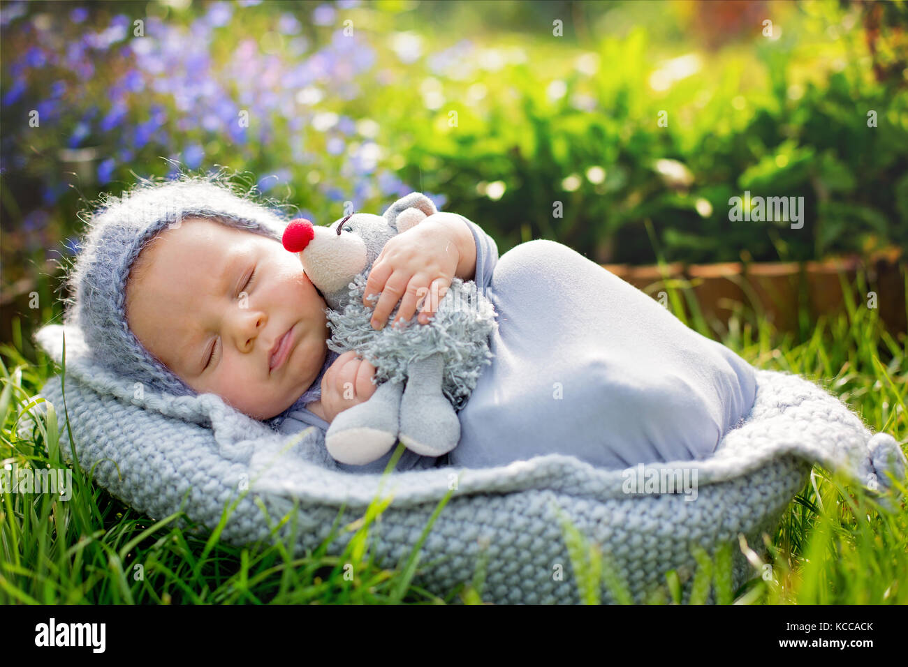 Cute little newborn baby boy, sleeping wrapped in gray wrap, holding cute  little mouse toy, outdoors in garden Stock Photo - Alamy