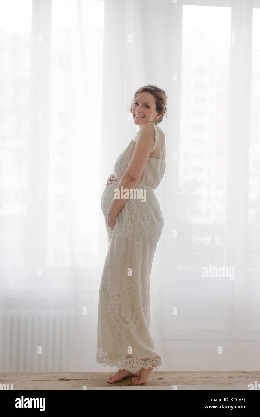 Elegant pregnant woman looking at camera on bench on a white background Stock Photo