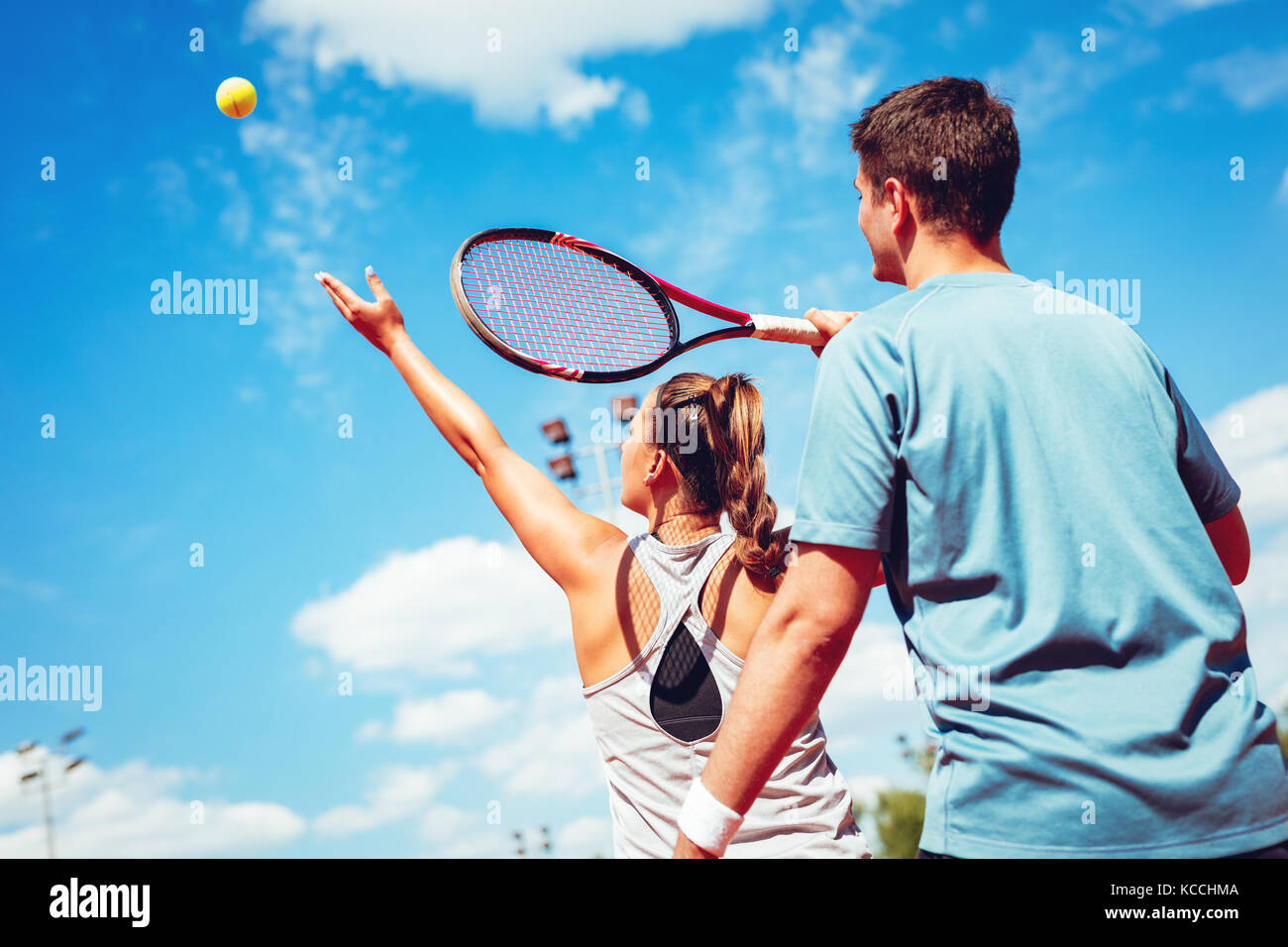 Beautiful young lefthanded woman with her trainer practicing serve on