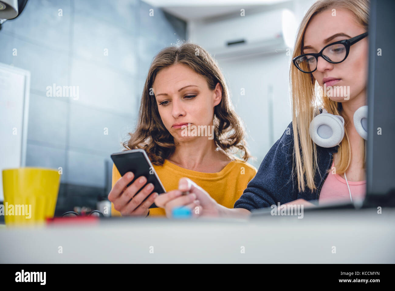 Two business woman working together at the office using smart phone and writing notes Stock Photo