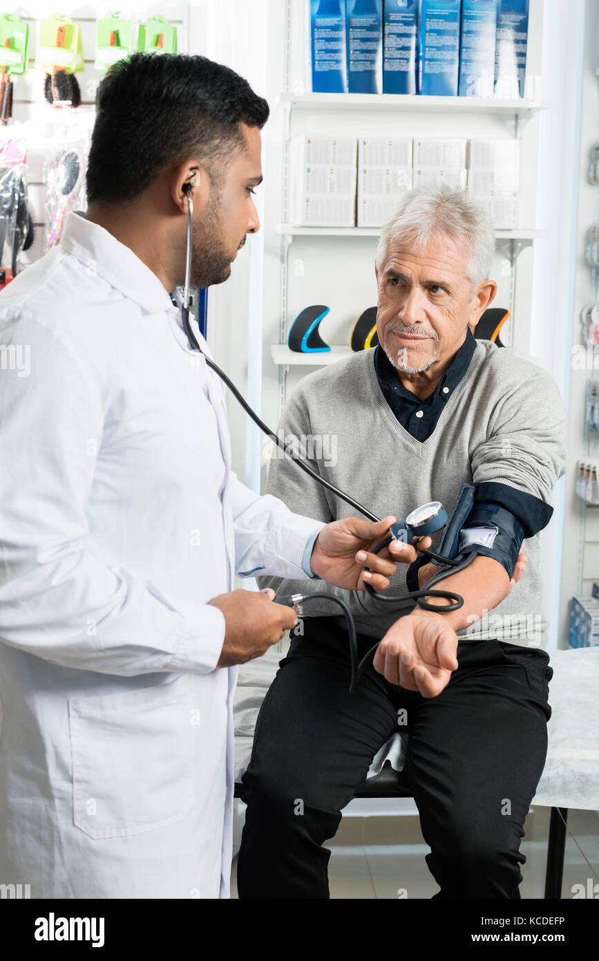 Senior male patient looking at chemist checking blood pressure in