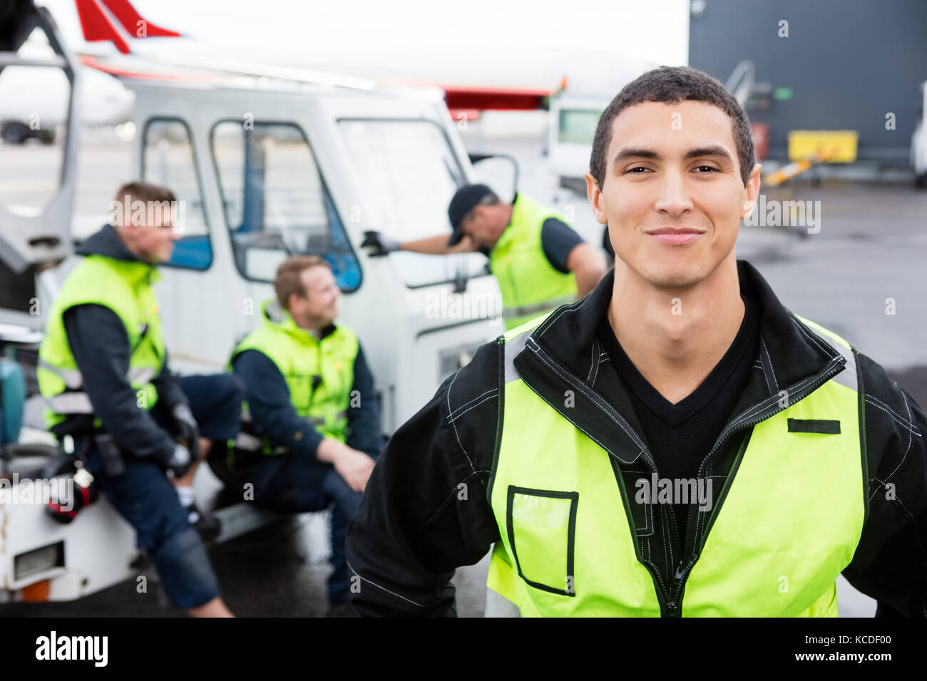 Portrait of confident male worker standing while colleagues communicating at gangway on runway Stock Photo
