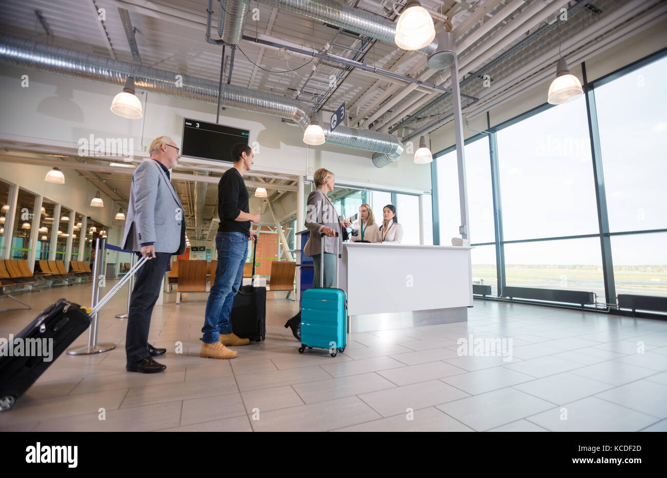 Low angle view of male and female passengers with luggage waiting at reception in airport Stock Photo