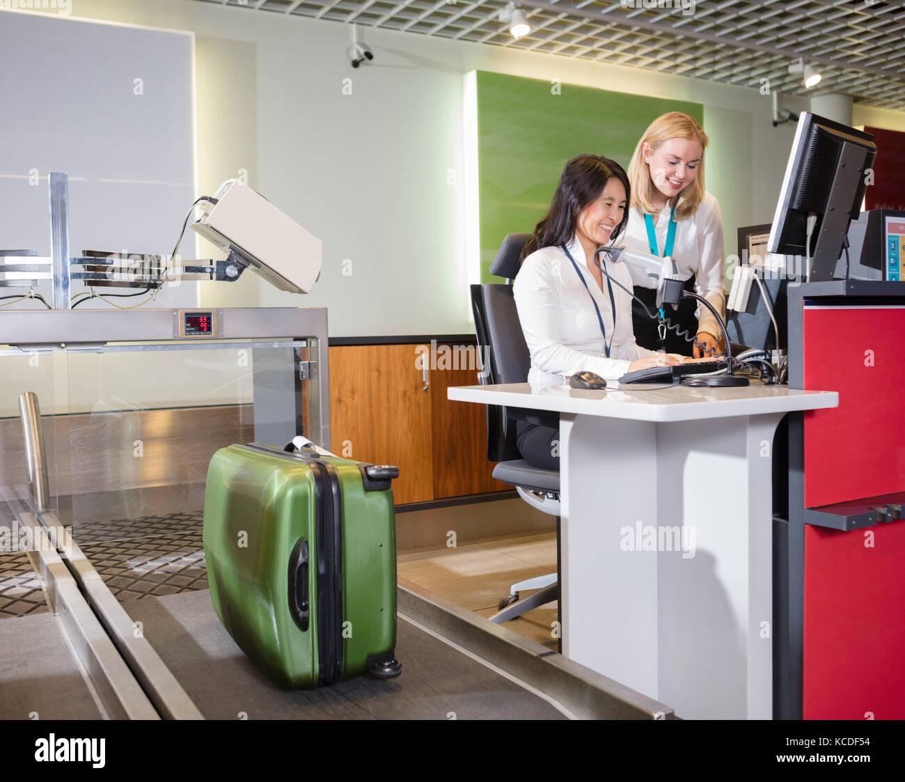 Smiling female staff weighing luggage at airport check-in desk Stock Photo