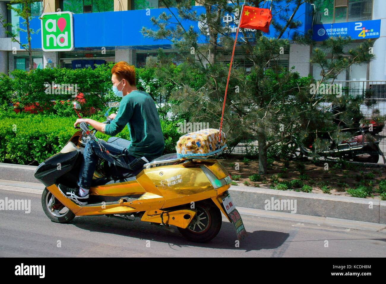 Fashionable young Chinese man teenager riding on scooter motorbike in Taiyuan China city centre road street wearing pollution facemask Shanxi Province Stock Photo
