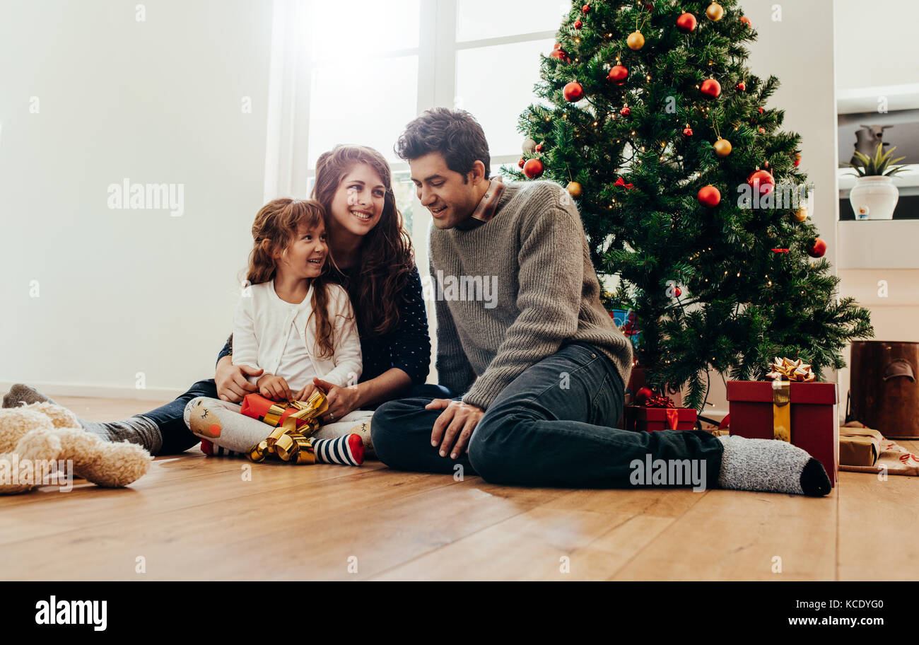 Family sitting beside Christmas tree opening gifts. Small family having happy time together on Christmas. Stock Photo