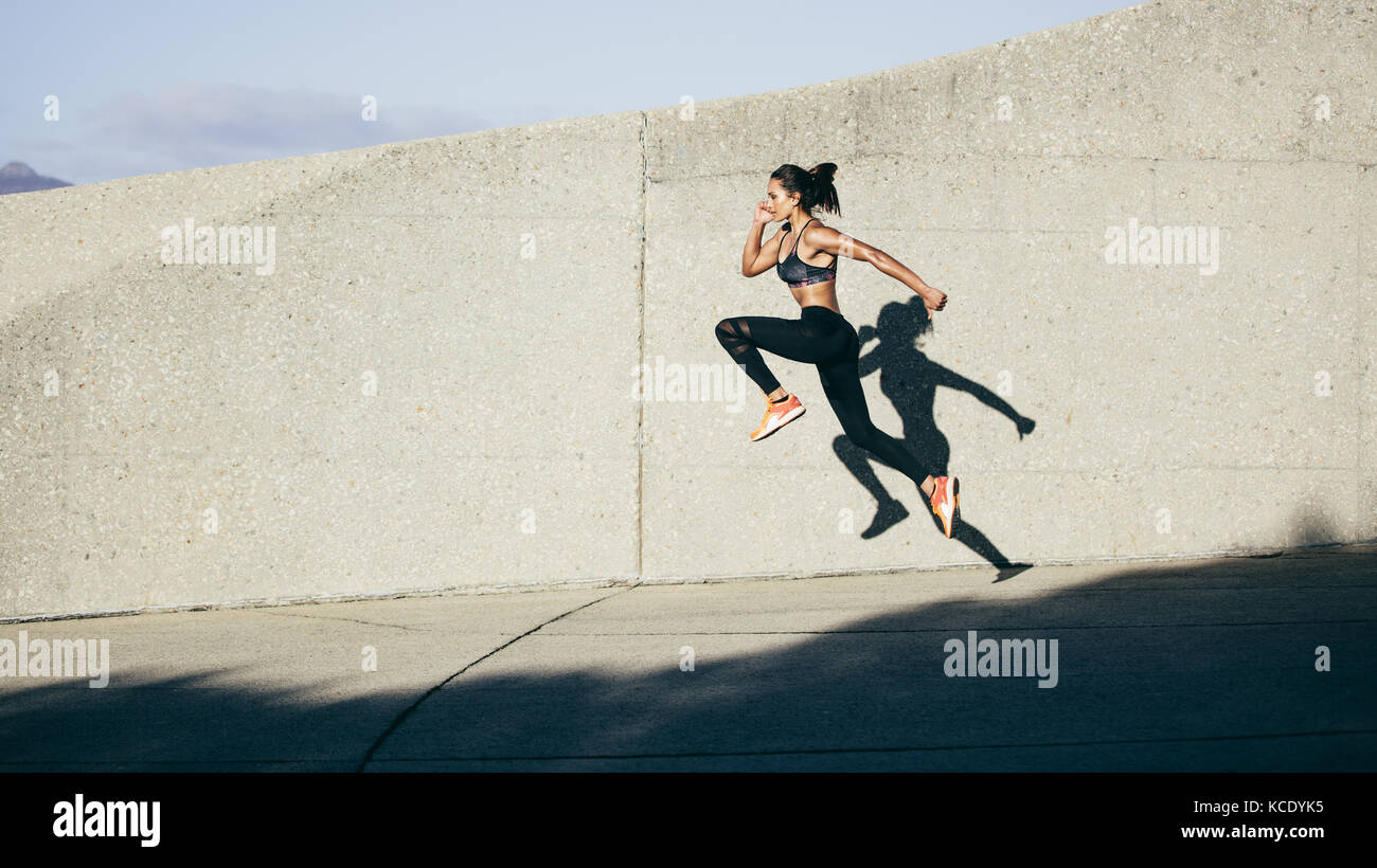 Athletic woman running and jumping outdoors. Muscular female exercising in morning. Stock Photo