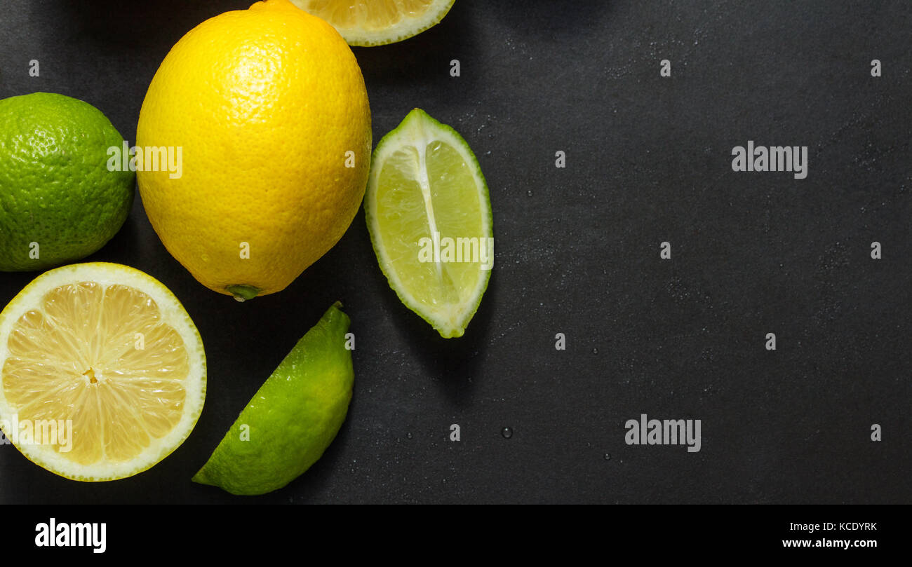 Cut and uncut limes and lemons on a black background. Top view of limes