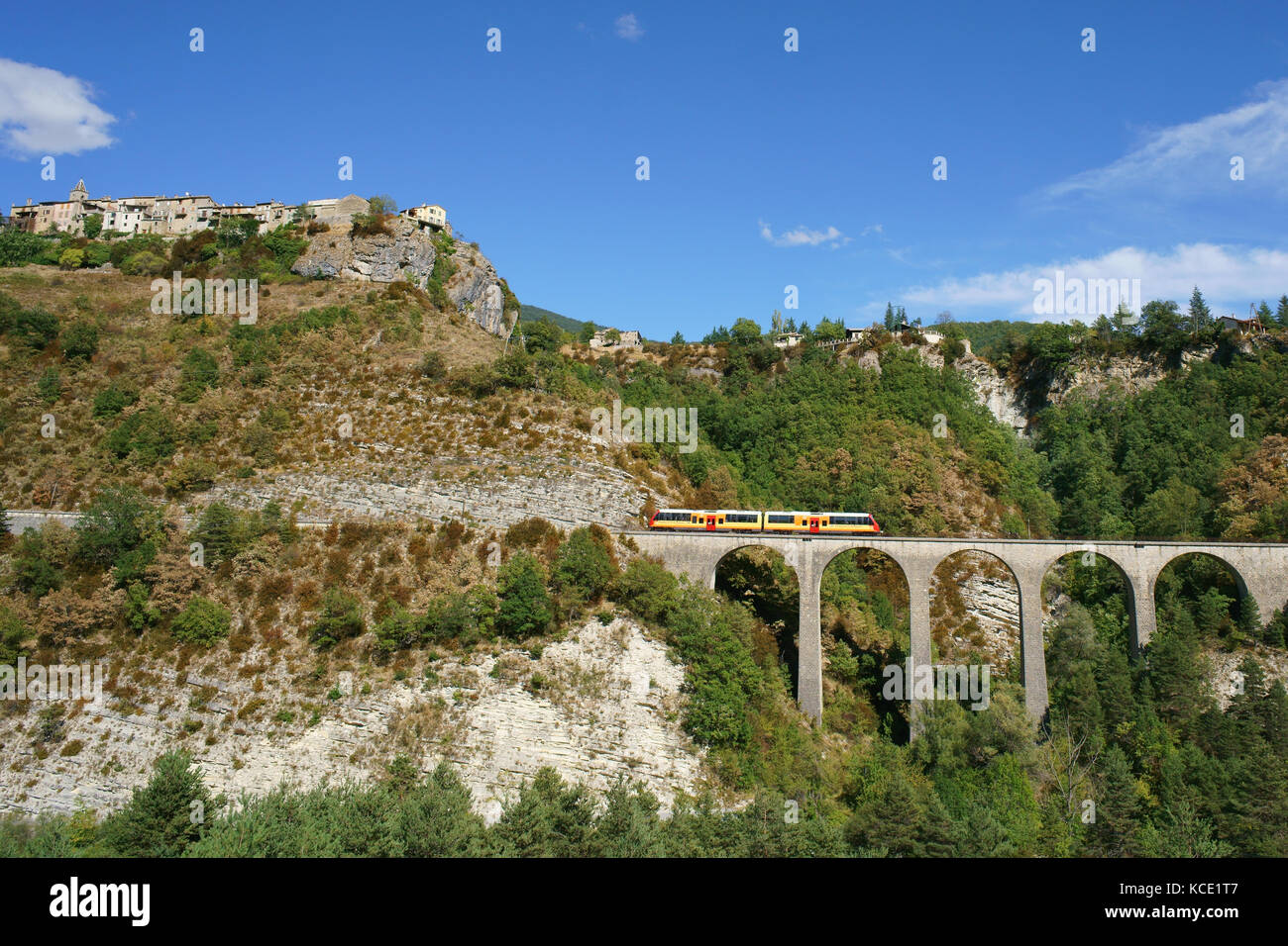 Picturesque landscape with a commuter train on a stone viaduct below a perched medieval village. Méailles, Alpes-de-Haute-Provence, France. Stock Photo