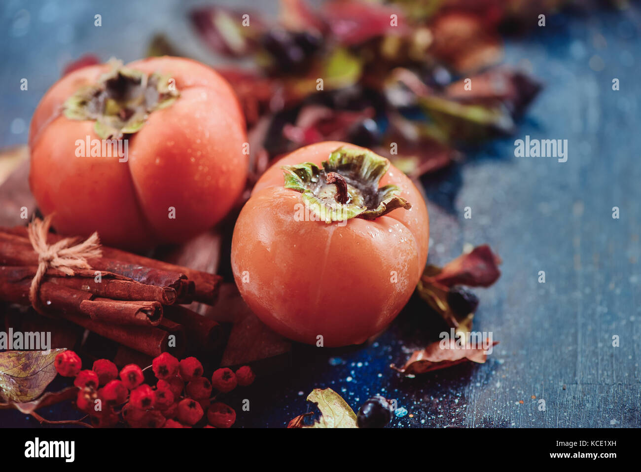 Ripe persimmons on a dark wooden background with autumn leaves, berries and cinnamon. Flat lay with copy space. Fruit in dark food photography. Stock Photo