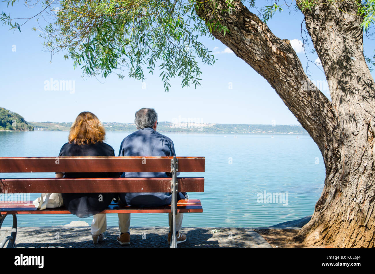 Rear shot of an elderly couple resting on a bench in the shade of a ...