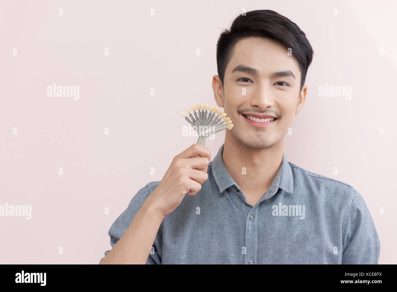 Asian male smiling while holding tooth color samples in his hand. Dental care and maintenance concept Stock Photo