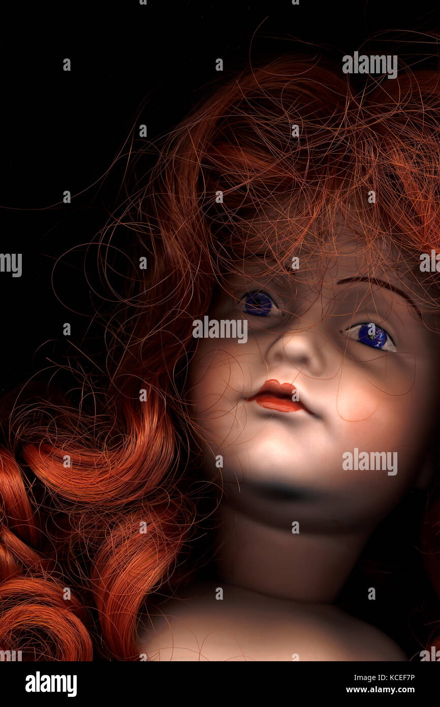 Extreme close-up of red-haired bisque dolls head, blue eyes, red lips. Attractive, enigmatic. Book cover, portrait Stock Photo