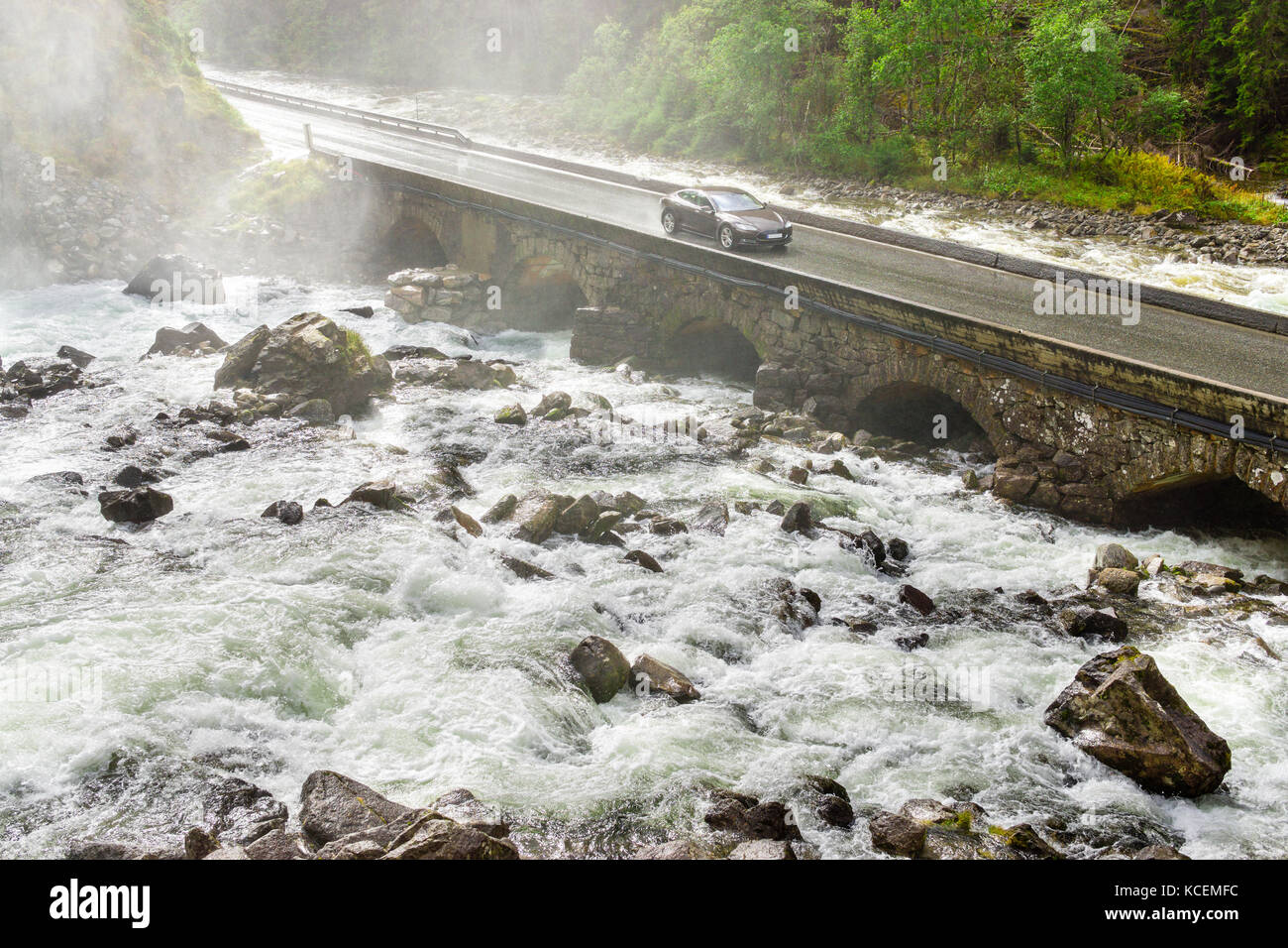 Electric car driving on bridge crossing river. Renewable energy from hydropower concept. Stock Photo